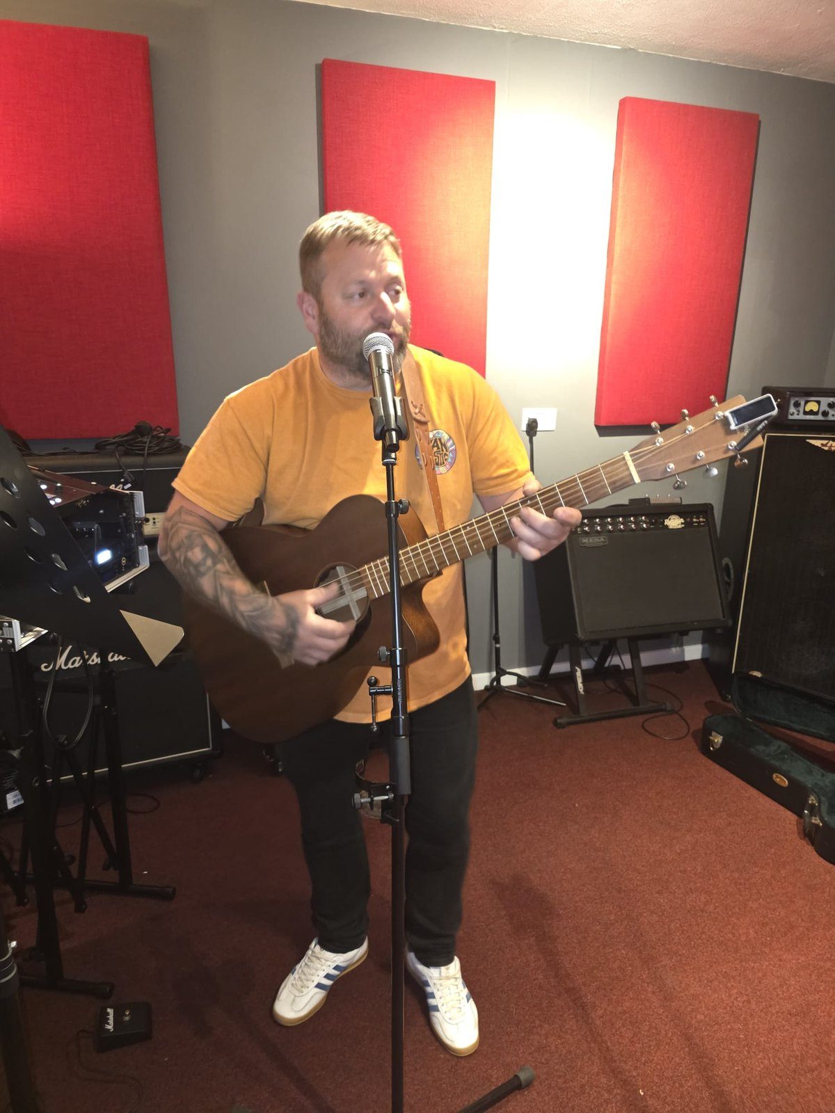 A Smashroom member singing into a microphone while playing an acoustic guitar in the live room
