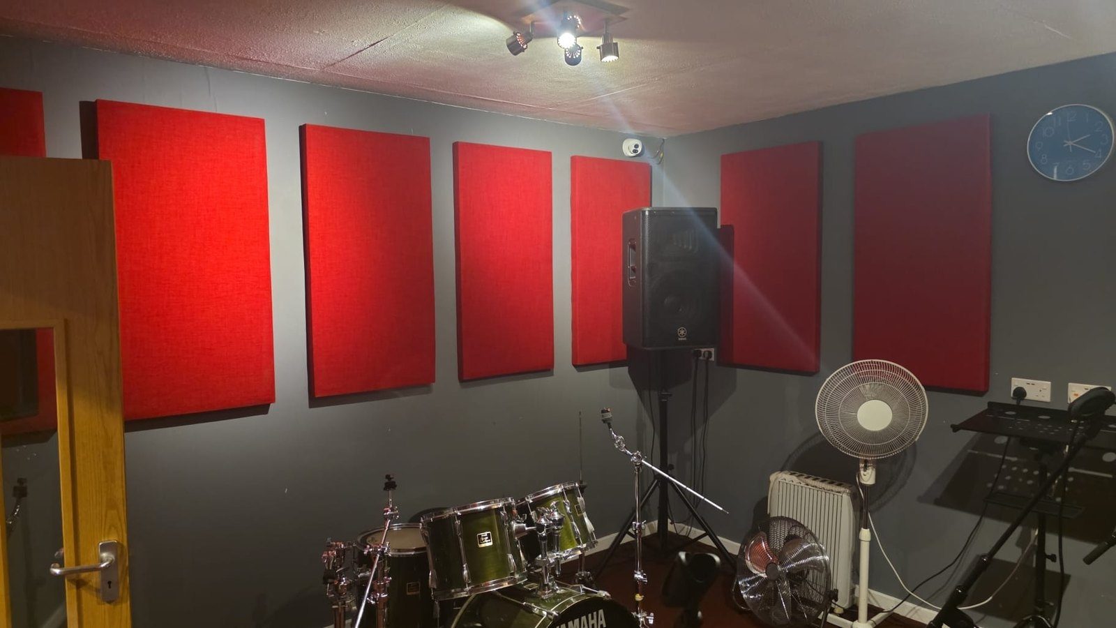 A full drum kit set up beside red acoustic panels and amplifiers in a Smashroom practice room
