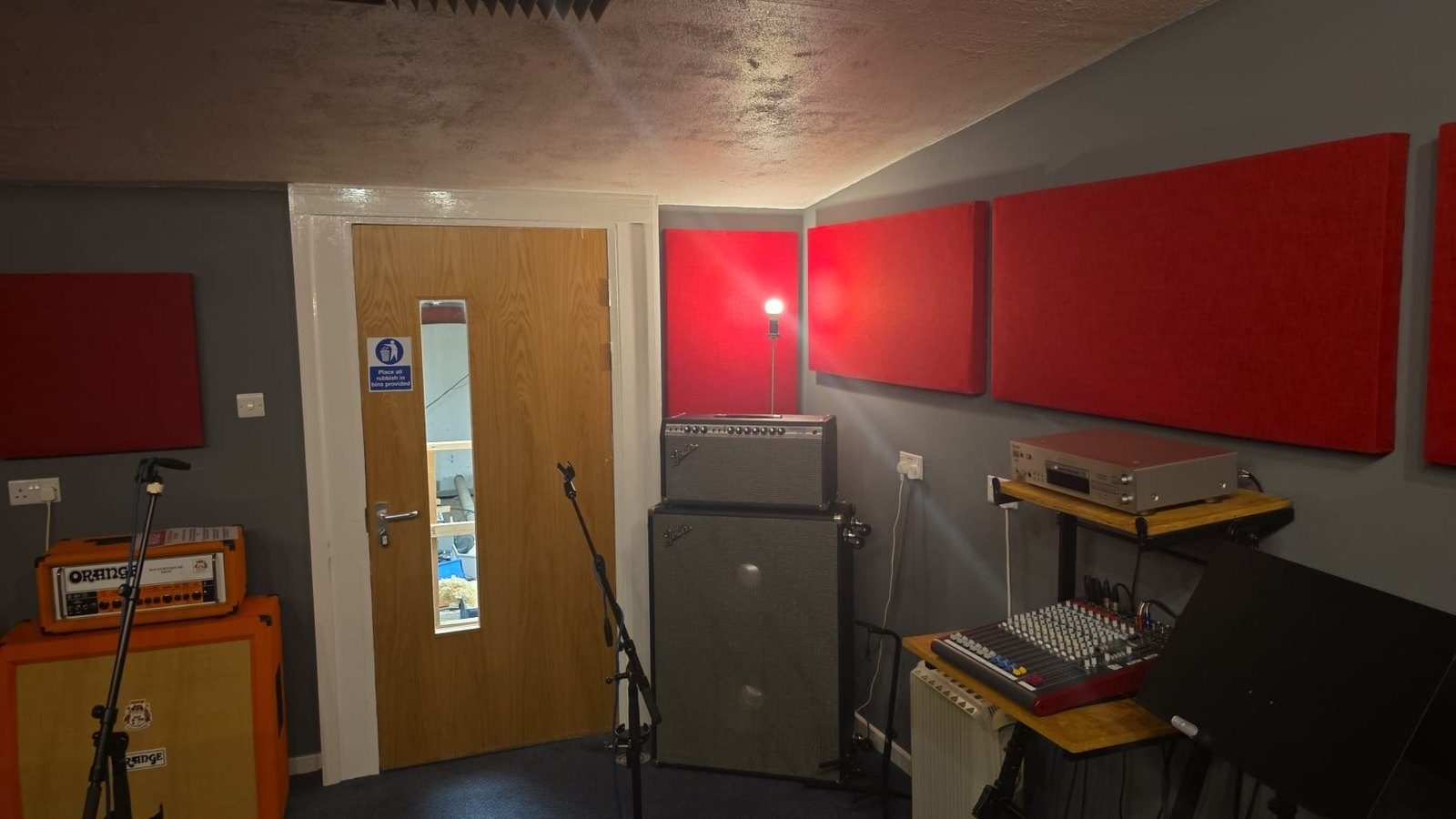 The main rehearsal room at The Smashroom with Fender and Orange amplifier stacks and red acoustic panels