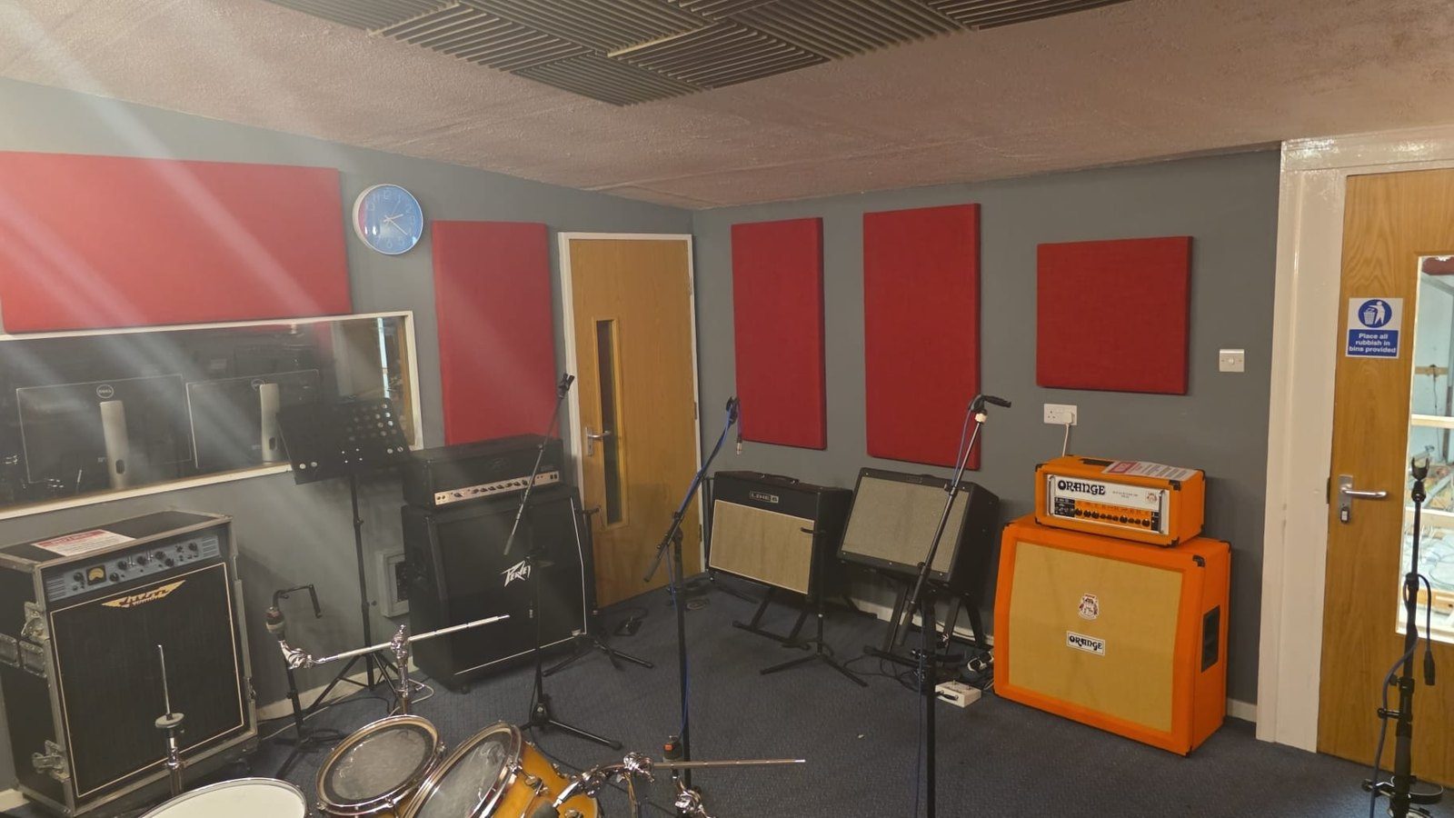 A wide view of a Smashroom rehearsal room with amplifiers, an orange amp, drums and red acoustic panels